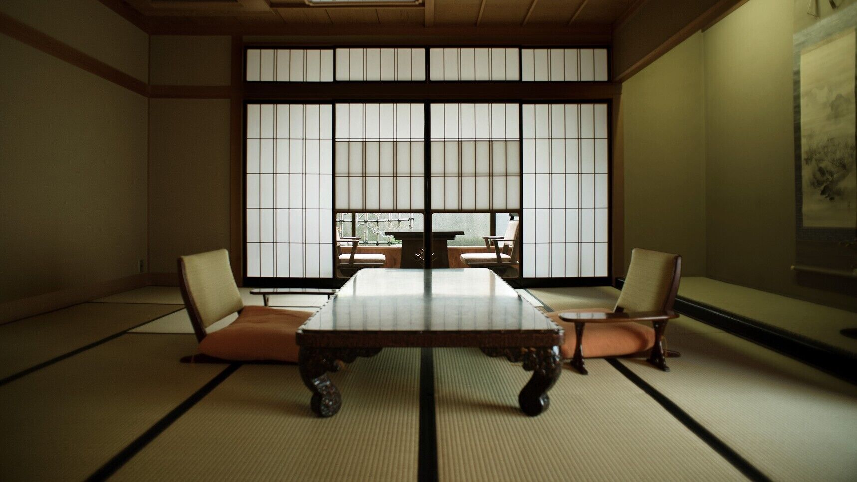 Una habitación con esteras de tatami, una mesa baja y dos sillas, amplios paneles shoji y vistas a través de ellos.