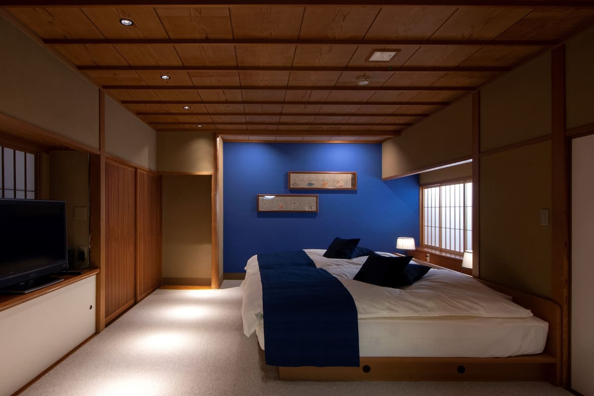 A bedroom with a bed, a television on a stand, a blue wall, and a window.
