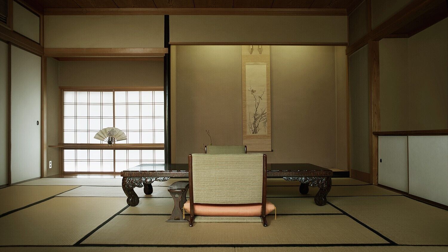 Una habitación con esteras de tatami, una mesa baja, una silla y un pergamino colgado.