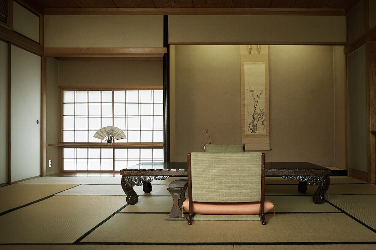 A tatami mat room with a low table, a chair, and a hanging scroll.