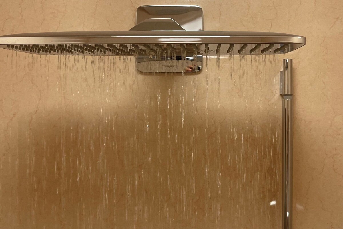 A shower with a rain-like water feature, a control panel, and a handheld showerhead.