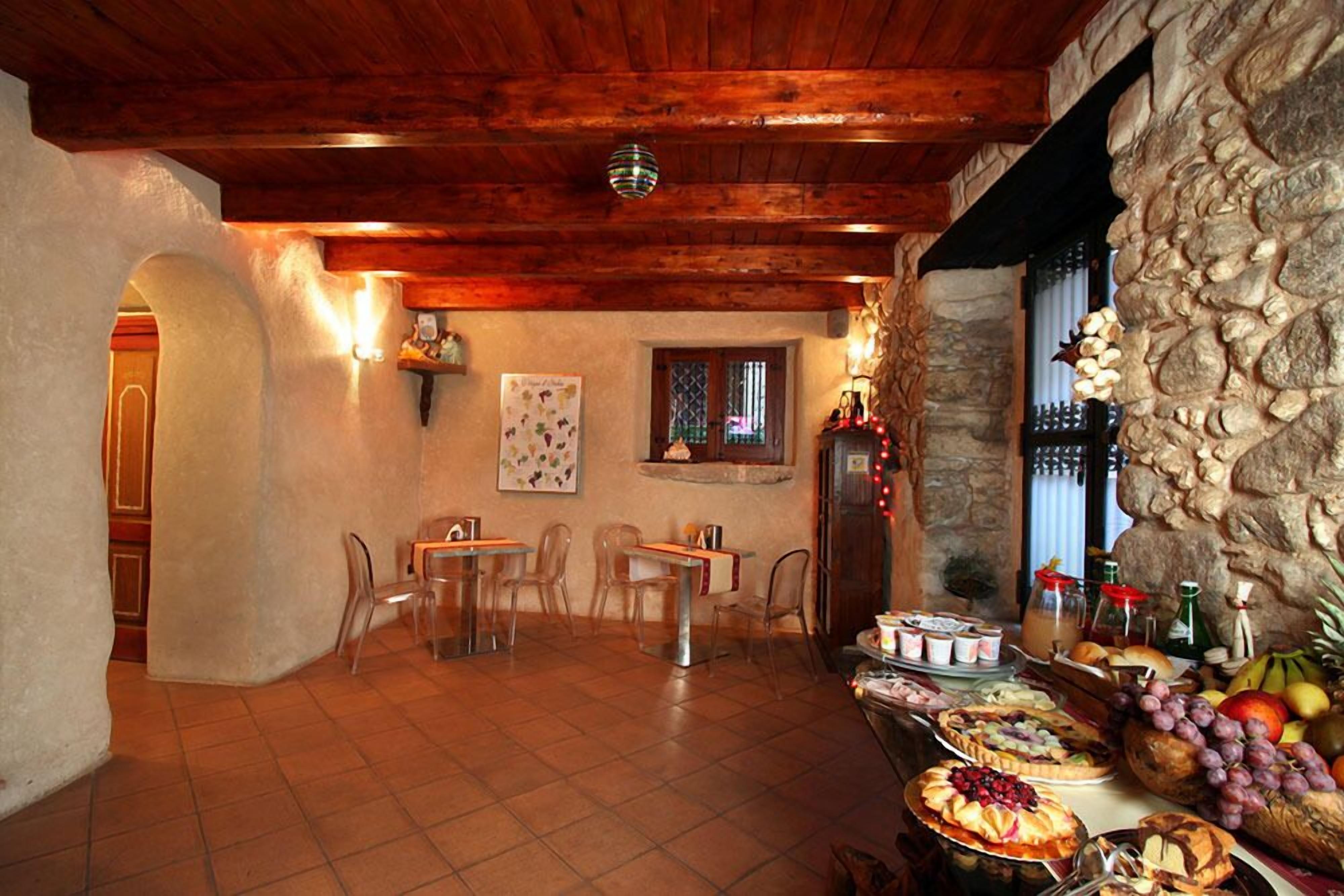 Un'area ristorazione rustica con pareti in pietra, travi in legno e una selezione di cibi esposti su un tavolo.