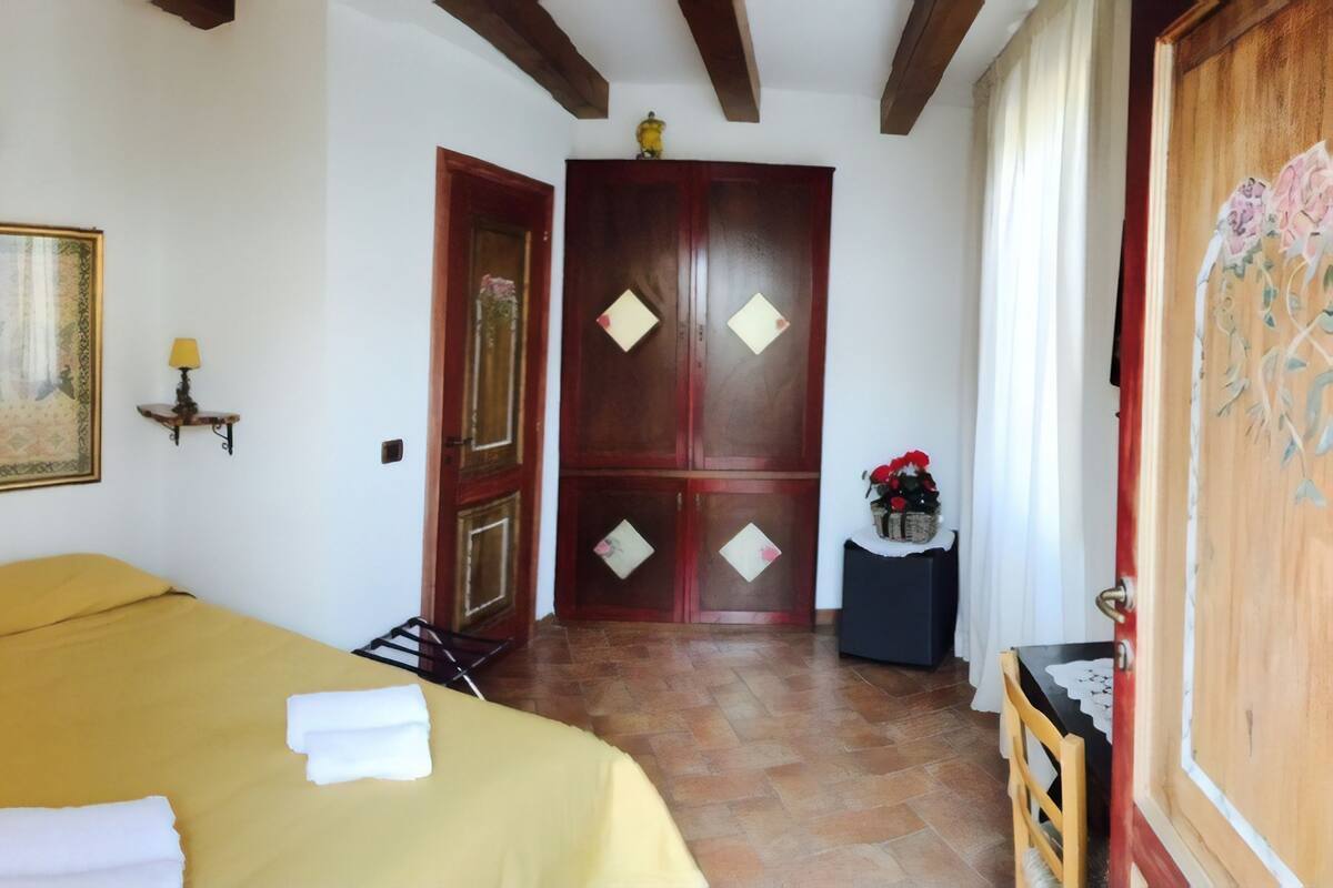 A hotel room with a bed, a large decorative mirror, a wooden wardrobe, and a small table with a vase of flowers.