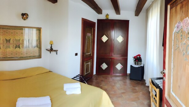 Habitación de hotel con una cama, un espejo decorativo grande, un armario de madera y una mesita con un florero.