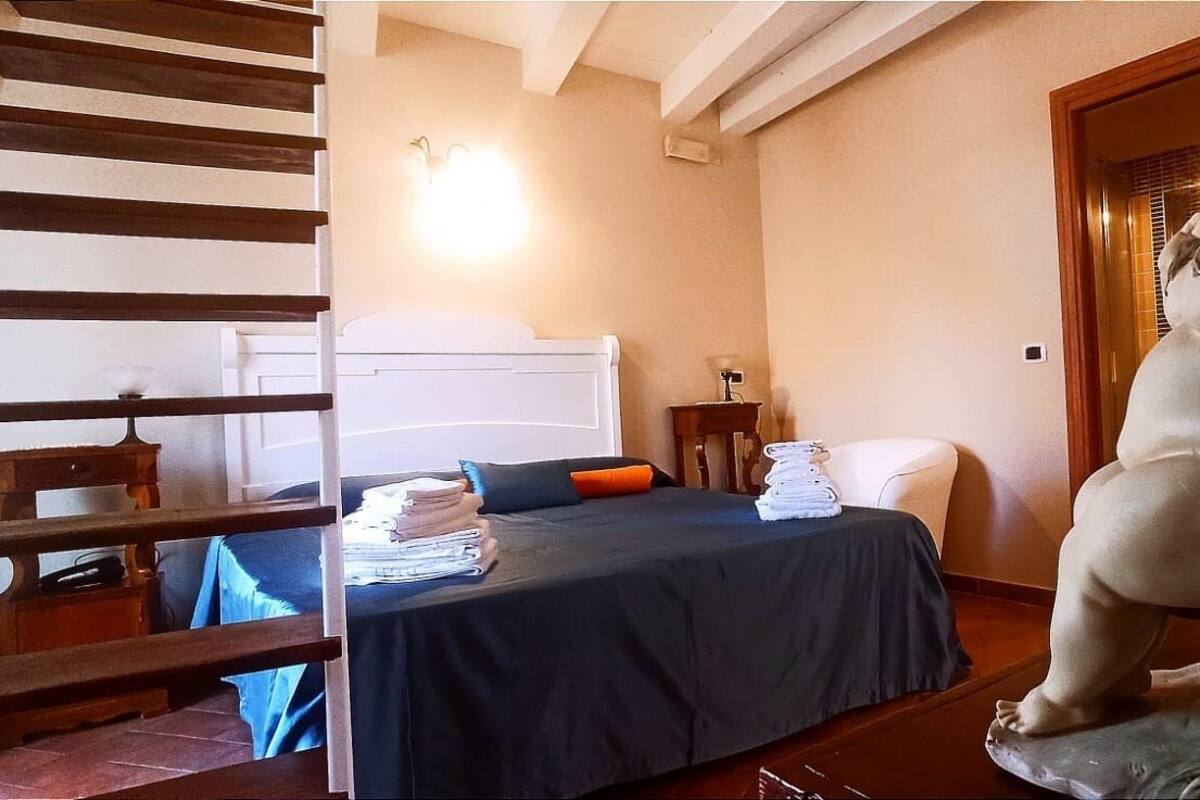 A bedroom with a bed, a wooden staircase, a statue, and a nightstand.