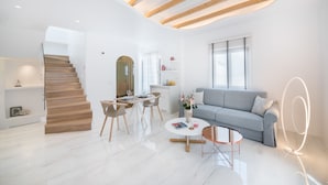 A modern living room with a staircase, a dining area, and a sofa. - Emfasis Villa (Santorini)