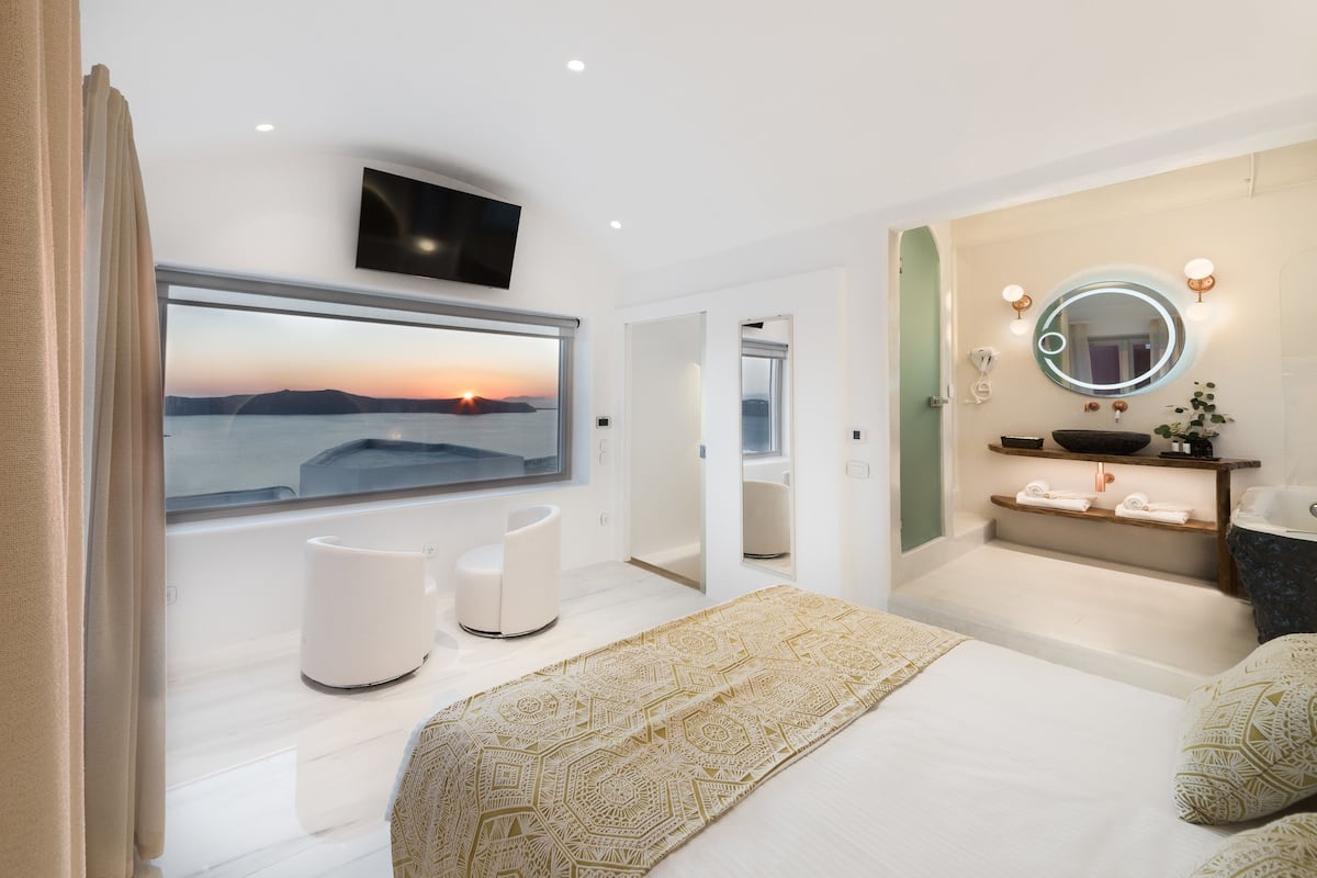 A modern bedroom with a large window, a bed, a bedside table, a mirror, and a television.