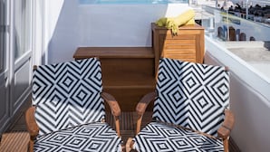 A balcony with two patterned chairs, a wooden table, and a view of the sea. - Emfasis Villa (Santorini)