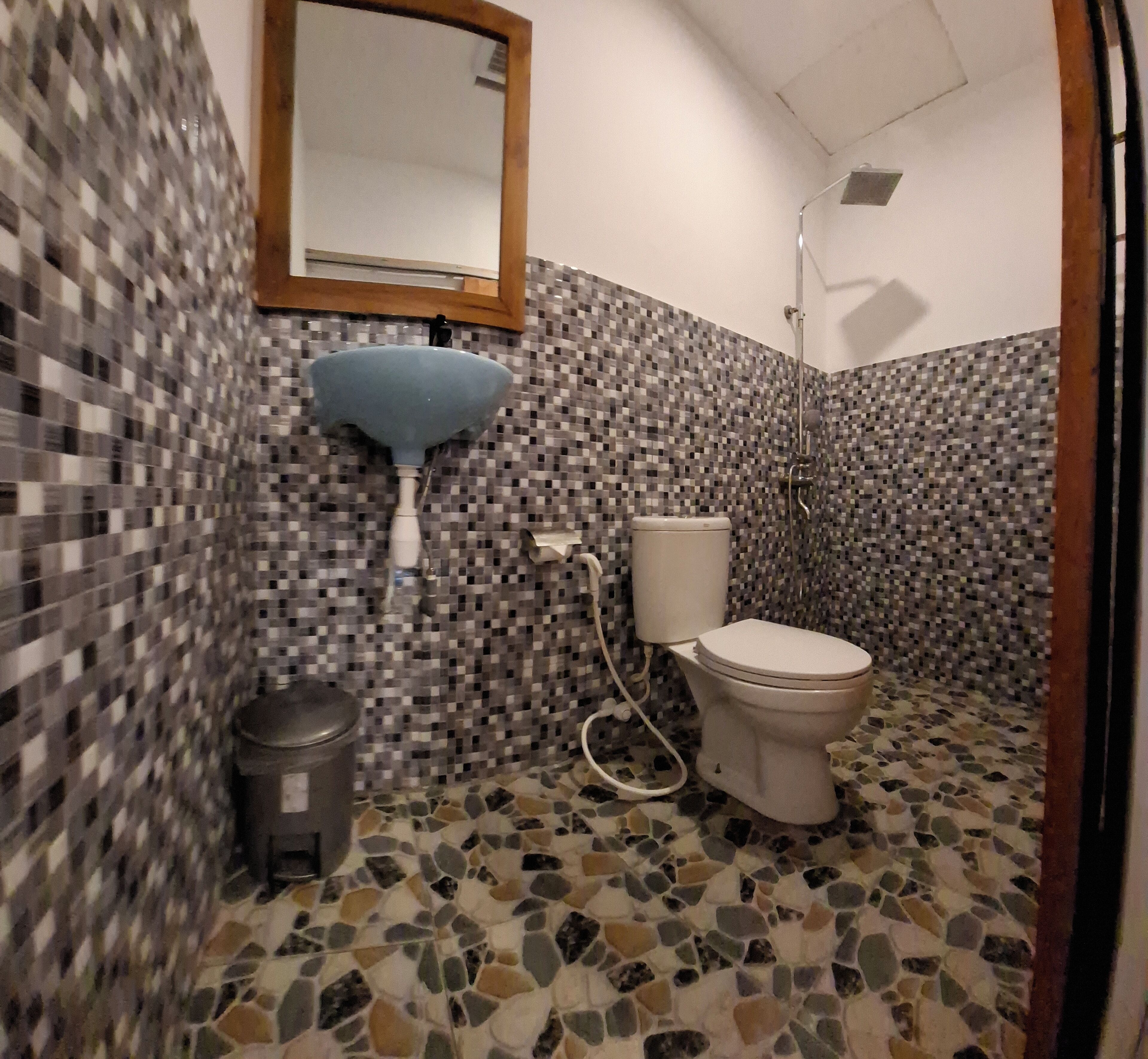 Une salle de bain avec des murs recouverts de mosaïques, un lavabo bleu, des toilettes et une douche.