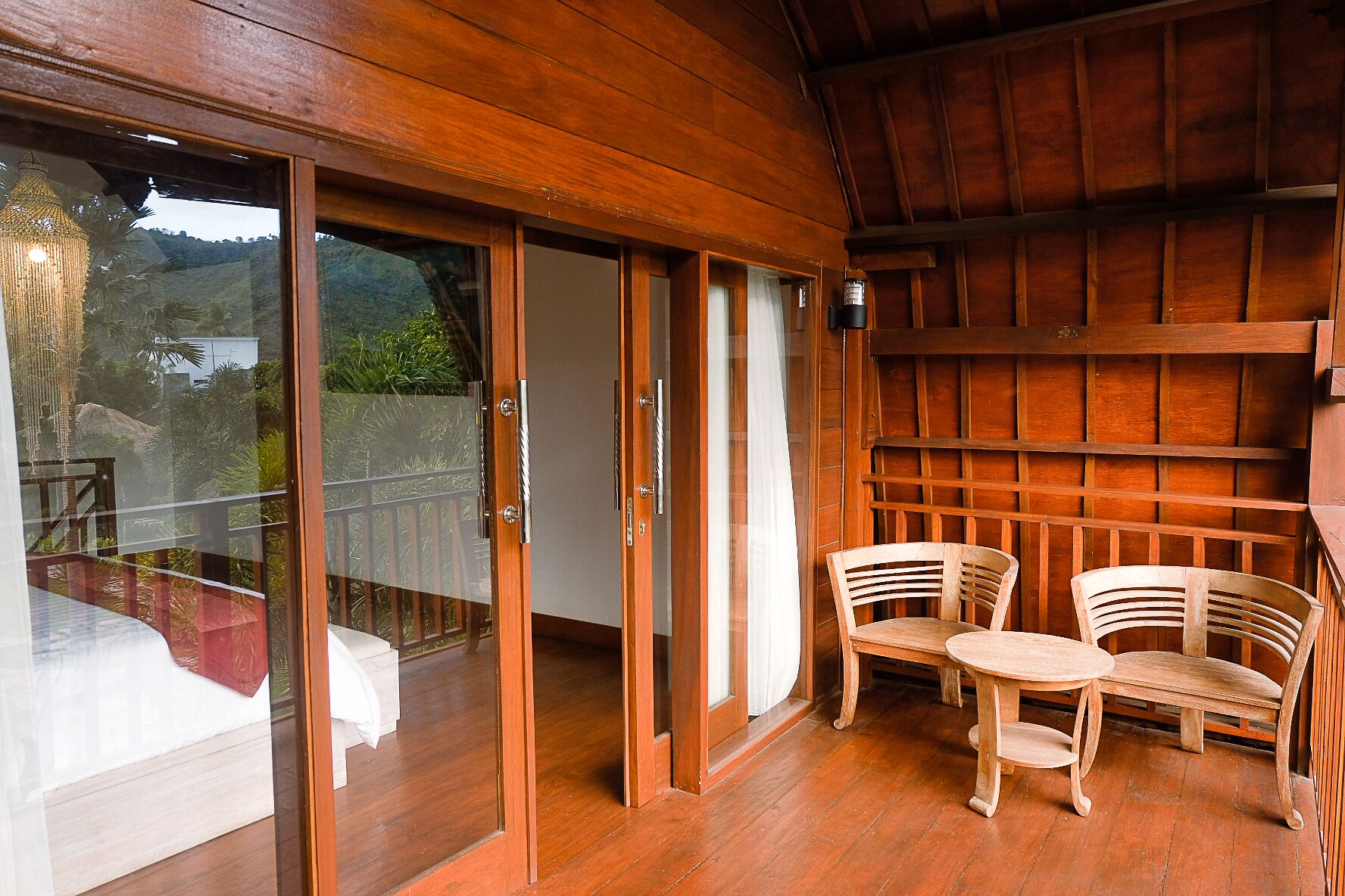 A wooden interior with sliding glass doors leading to a balcony, two wooden chairs, and a small round table.