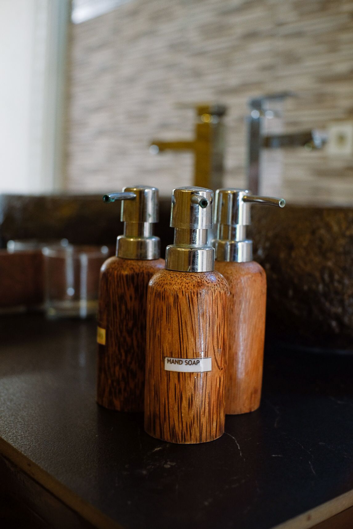Three wooden hand soap dispensers with metal tops on a countertop.
