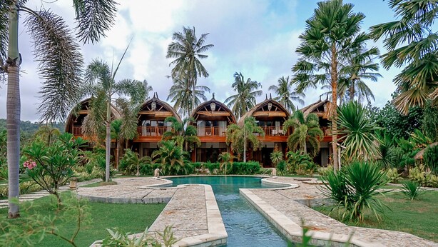 Un resort con varias villas de madera, una piscina central y exuberante jardinería tropical.