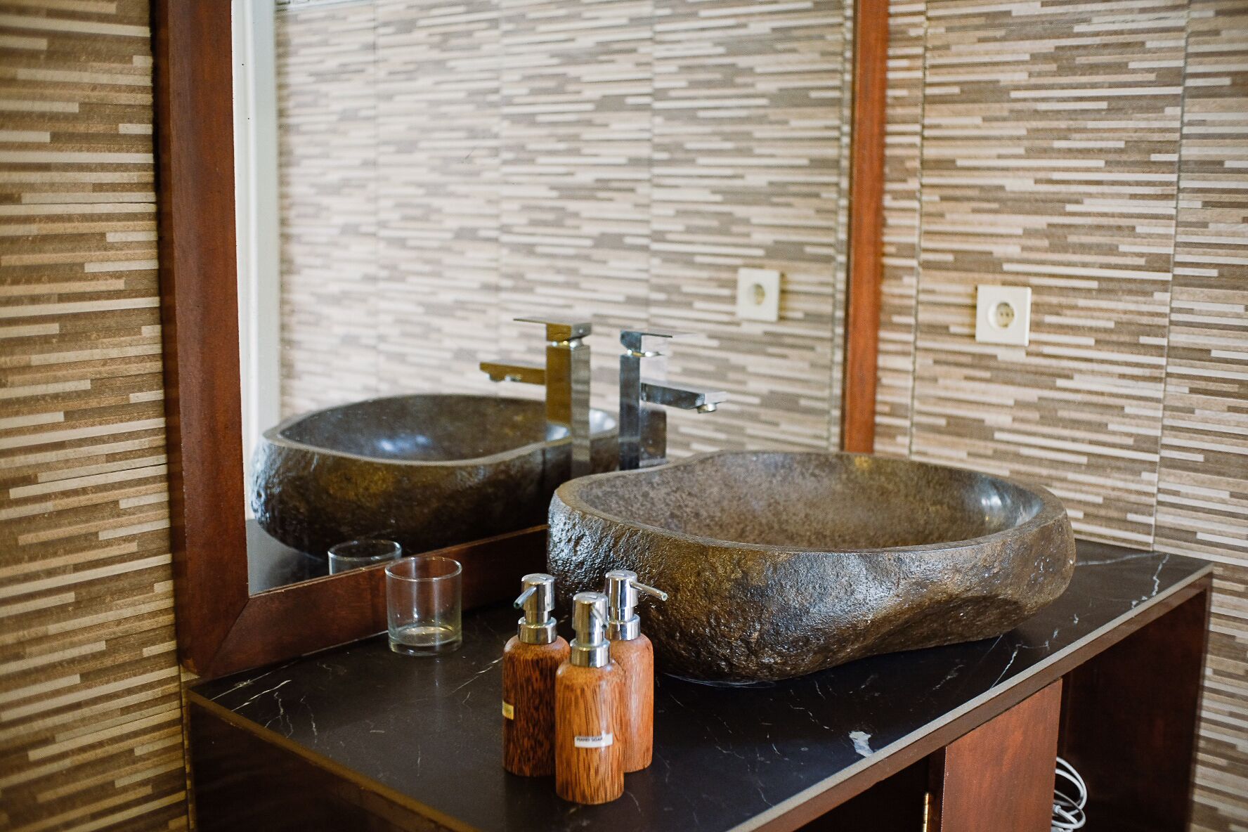 A bathroom with a large, round stone sink, a wooden countertop, and a mirror reflecting the sink and wall.