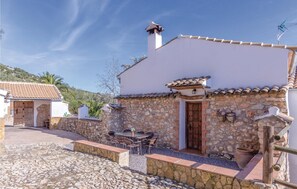 Un bâtiment en pierre avec un toit en tuiles, une porte en bois et une terrasse aménagée avec du mobilier d’extérieur.