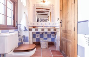 Une petite salle de bain avec des toilettes en bois, un lavabo surmonté d’un miroir décoratif et un mur recouvert de carreaux.