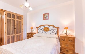 Une chambre à coucher avec un lit en bois, deux tables de chevet avec des lampes, une armoire en bois et un tableau encadré au mur.