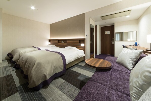 A hotel room with two beds, a sofa, a round table, and a mirror.