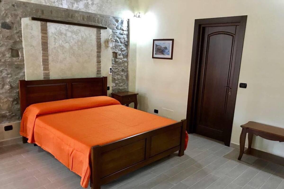 A bedroom with a wooden bed, a stone accent wall, a door, and a small bedside table.