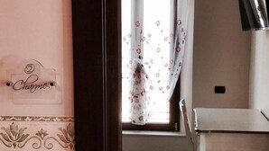 A room with a dining table and chairs, a window with floral curtains, and a wall with a decorative border and a sign that reads "Charmes". - Eleven Bed & Breakfast (Reggio Calabria)