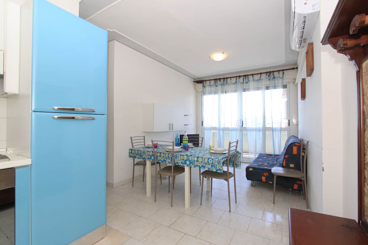 A dining area with a blue refrigerator, a table with chairs, and a sofa.