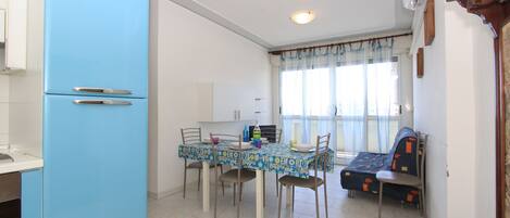 A dining area with a blue refrigerator, a table with chairs, and a sofa.