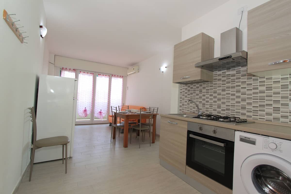 A modern kitchen with a built-in oven, a washing machine, and a dining area with a table and chairs.