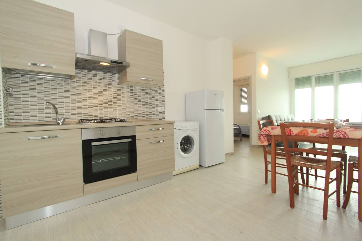 A modern kitchen with a built-in oven, a washing machine, and a dining area with a table and chairs.