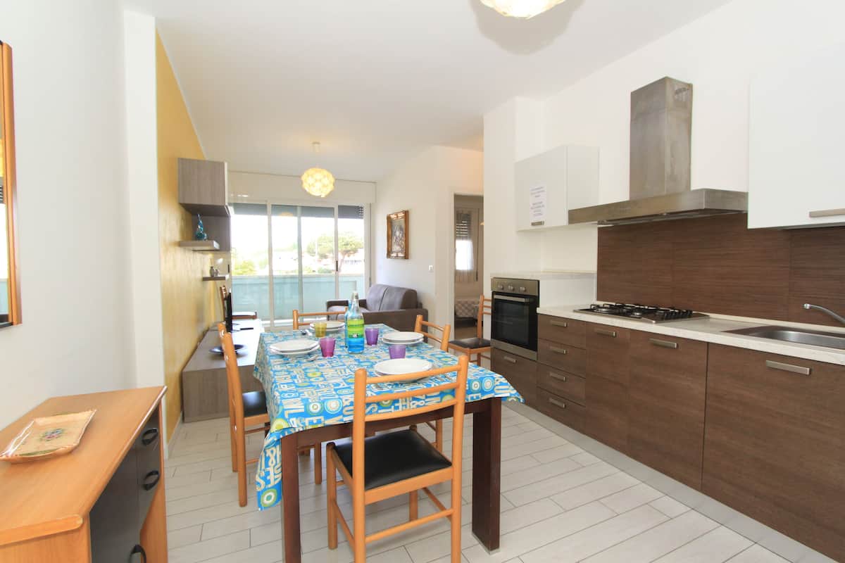 A modern kitchen with a dining table set for four, a built-in oven, and a large window offering a view of the outdoors.