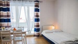 A room with a bed, a table with chairs, a window with curtains, and a lamp. - Family Homes - Apartamenty Vento (Wladyslawowo)