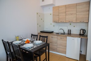 Une cuisine de taille réduite, avec des meubles en bois, un réfrigérateur blanc et une table à manger mise avec des assiettes, des verres et un panier de fruits.