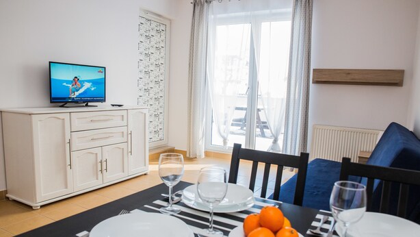 A dining area with a table set for four, a television on a cabinet, and a window with curtains. - Family Homes - Apartamenty Vento (Wladyslawowo)