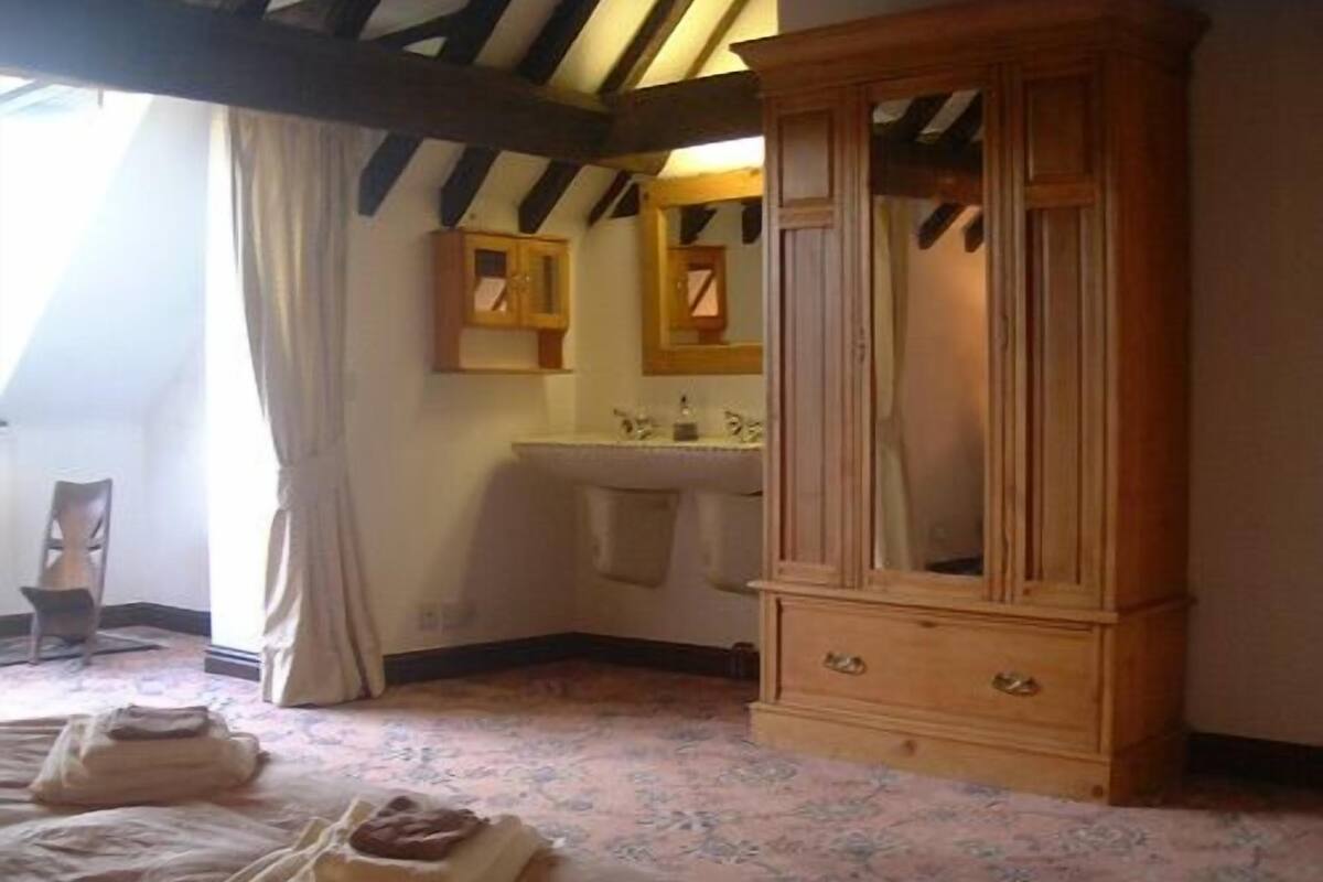 A bedroom with a wooden cabinet, a bed with a blanket, a chair, and a window with curtains.