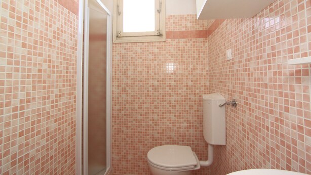 Un baño con mosaicos rosas, un inodoro y una ventana sobre el lavabo.