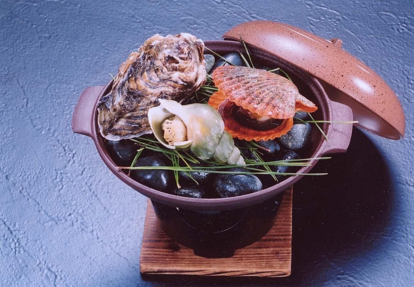 A ceramic pot with various seafood items on a wooden board.
