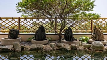 A tranquil garden with a pond, stone sculptures, and a bamboo fence.