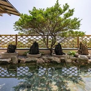 A tranquil garden with a pond, stone sculptures, and a bamboo fence. - Shima Beach Hotel (Toba)