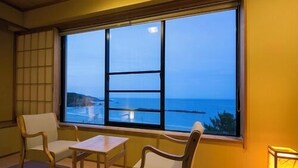 Una habitación con un ventanal grande, dos sillas, una mesita y una lámpara.