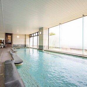 Une piscine intérieure à l’eau claire, aux murs carrelés et à l’intérieur baigné de lumière naturelle.