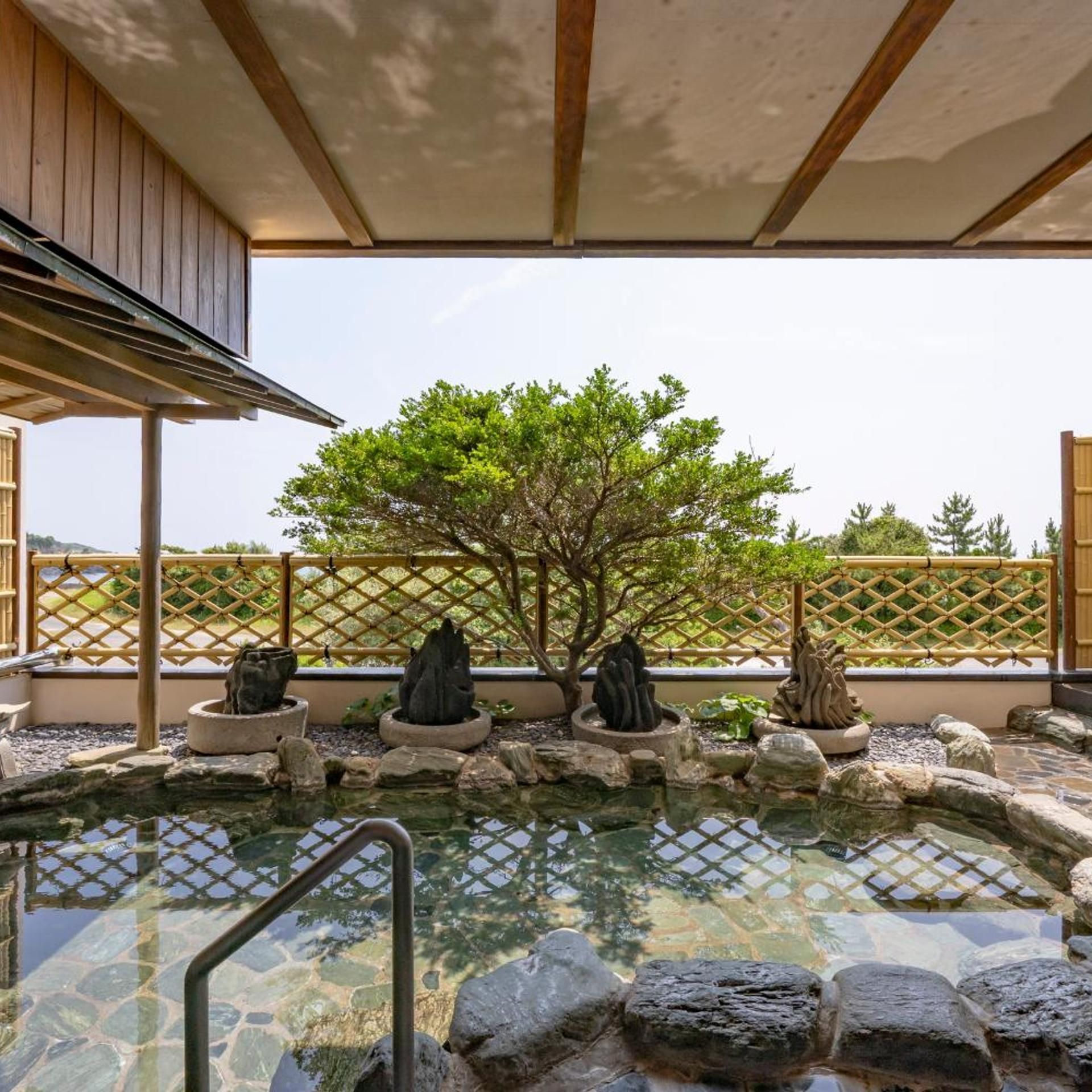 Un jardin japonais traditionnel avec un bassin en pierre, des formations rocheuses et une clôture en bambou.
