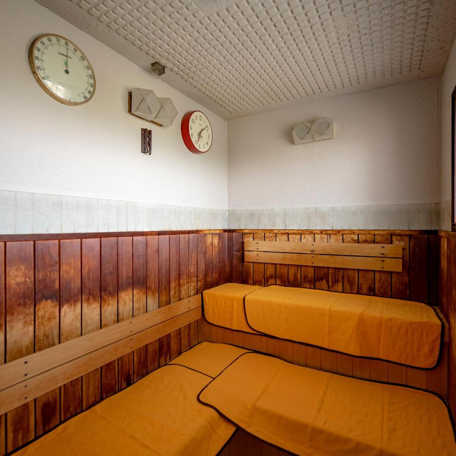 A room with wooden paneling, two beds with yellow covers, and three clocks on the wall.