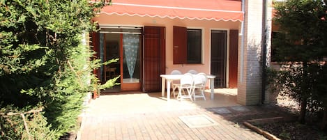 A patio area with a brick floor, a table with chairs, and a red awning.