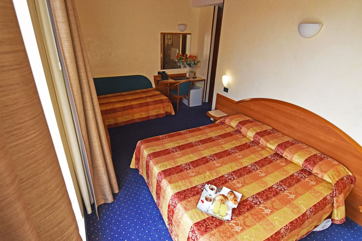 A hotel room with two beds, a desk, a chair, and a mirror.