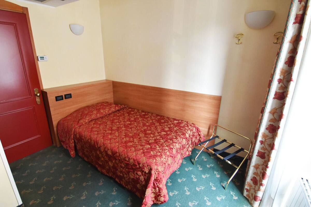 A small, single-bed room with a wooden headboard, a red door, and a curtain with a floral pattern.