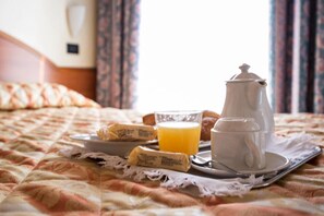 A breakfast tray with croissants, a glass of orange juice, and a coffee pot on a bed with a patterned bedspread. - Hotel Brennero (Bassano del Grappa)