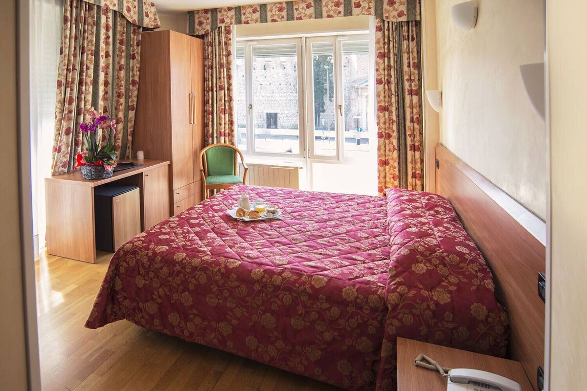 A bedroom with a bed, a desk, a chair, and a window with curtains.
