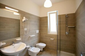 Ein Badezimmer mit einem Bidet, einer Toilette, einem Waschbecken und einer Duschkabine aus Glas.