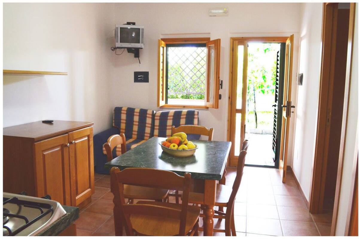 A compact kitchen with a dining table, chairs, a small TV, and a window with a view of greenery.