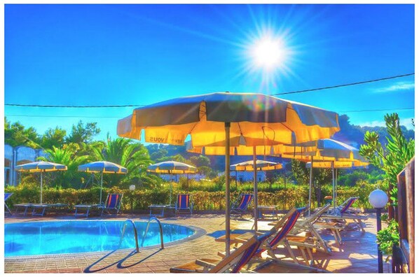 Ein Poolbereich mit mehreren Sonnenschirmen, Liegestühlen und blauem Himmel.
