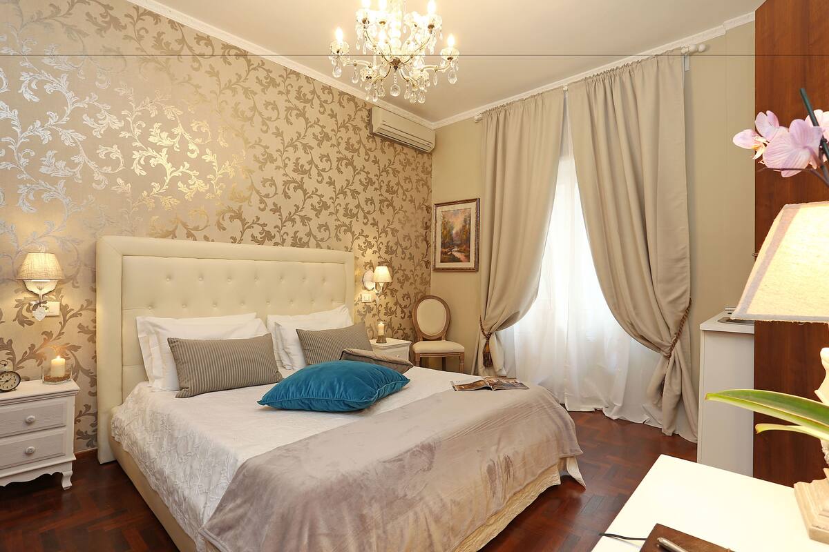 A well-appointed bedroom with a large bed, a chandelier, and a nightstand with a lamp.
