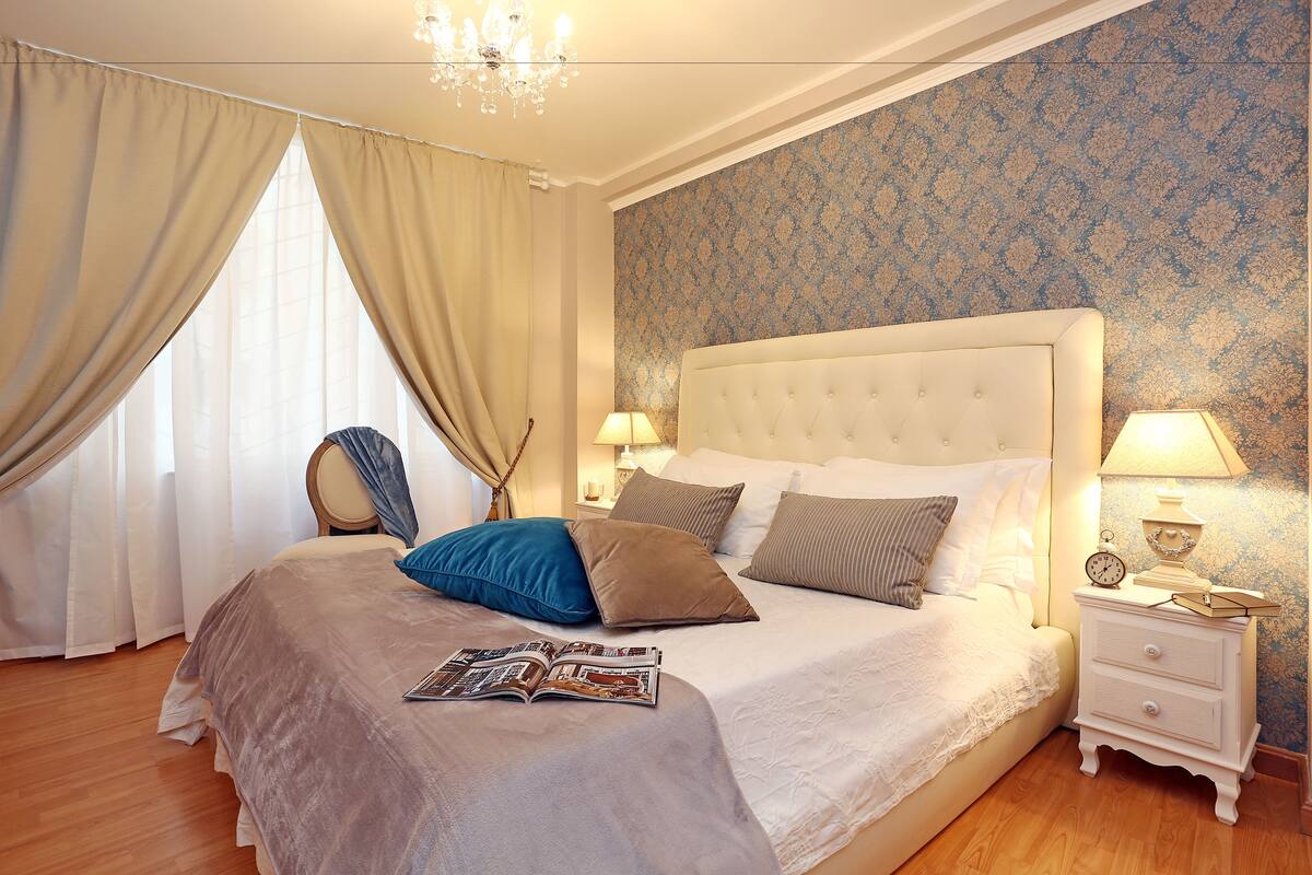 A neatly made bed with a magazine, a bedside lamp, and a clock on a nightstand.
